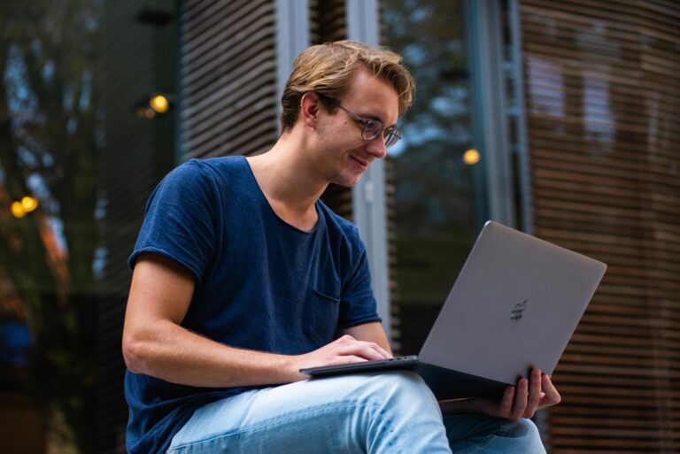 A young man sitting outdoors in Leiden, Netherlands, working on a laptop doing financial forecasting.